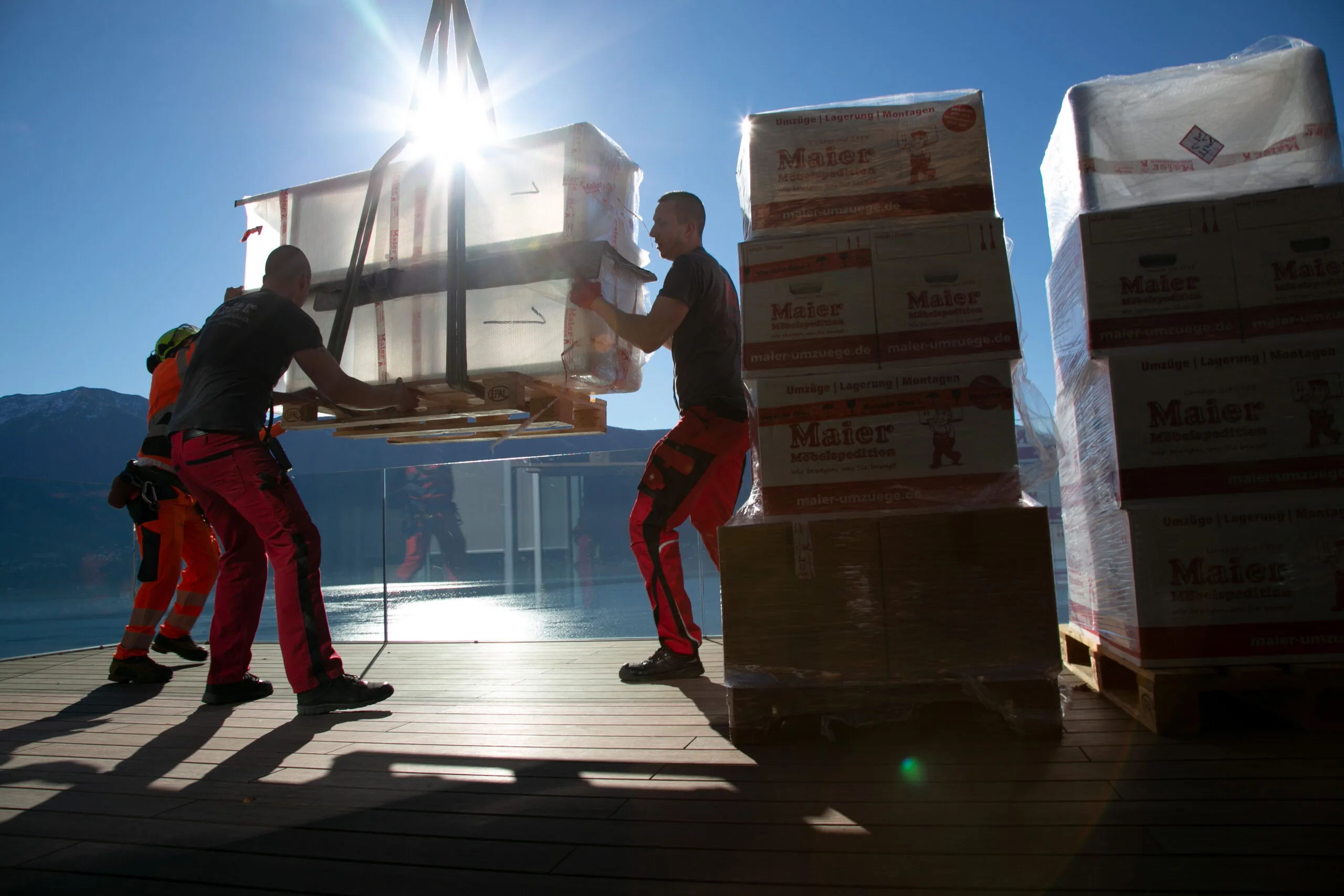 Removal workers unload pallets of goods against a breathtaking mountain backdrop and bathe in the warm glow of the sun.
